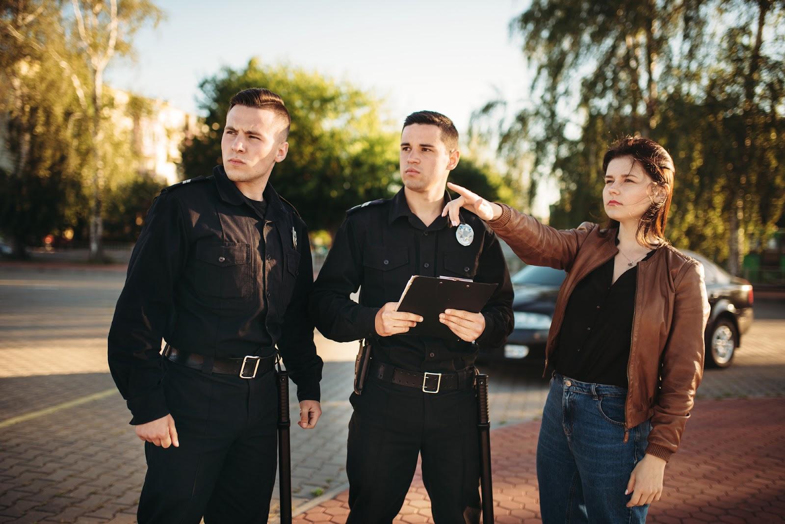 Two uniformed male police officers listen as a dark-haired woman points and answers questions after they have stopped her for reasonable suspicion.