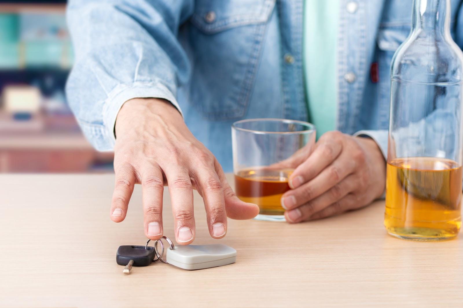 Man reaching for keys while finishing an alcoholic beverage, a choice that may lead to a DWI conviction